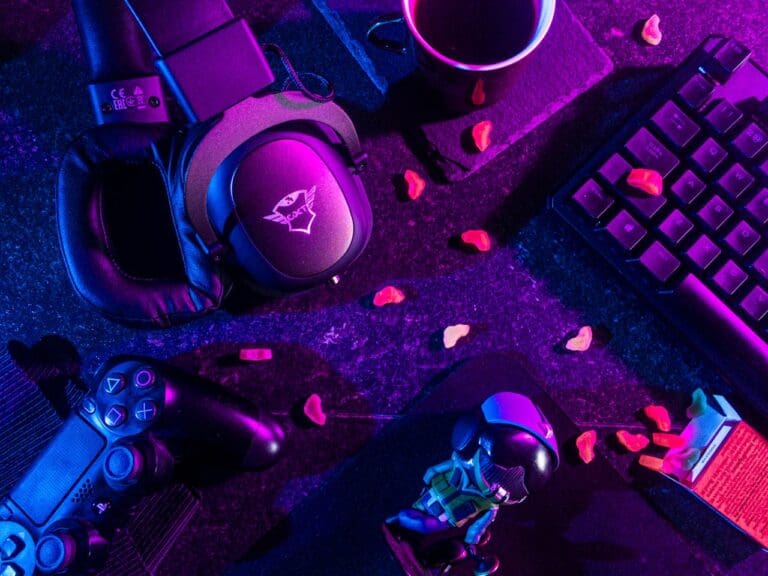 A gaming setup with a keyboard, headphones, PlayStation controller, coffee cup, small figurine, and scattered gummy candies under purple and blue lighting creates a cozy atmosphere—perfect for unwinding after a Brooklyn Therapy session or connecting with your therapist in NYC.