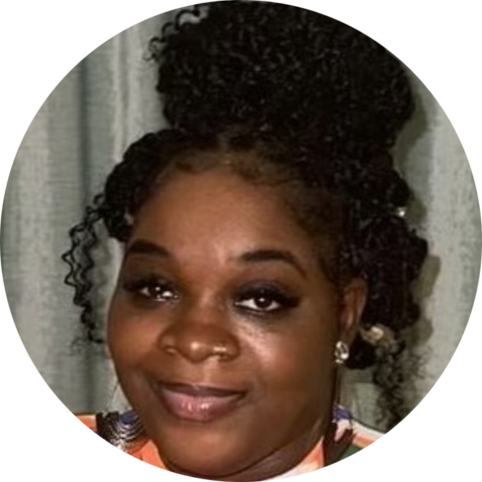 A woman with curly hair styled in a high bun, wearing makeup and earrings, smiles at the camera against a curtain background, embodying the warmth and approachability often associated with a therapist NYC or Brooklyn Therapy professional.