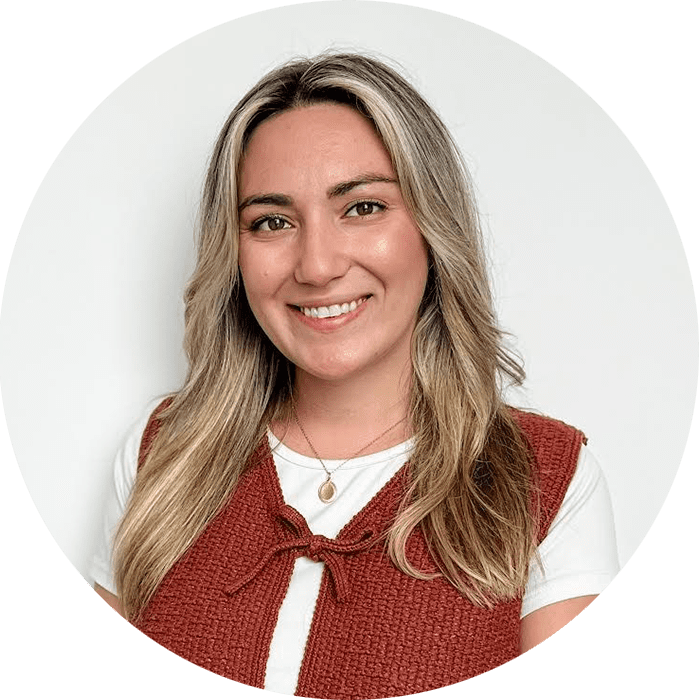 Woman with long blonde hair and a white shirt under a reddish-brown vest, smiling in front of a plain white background—an approachable therapist NYC residents trust, dedicated to providing compassionate Brooklyn Therapy to support your well-being.