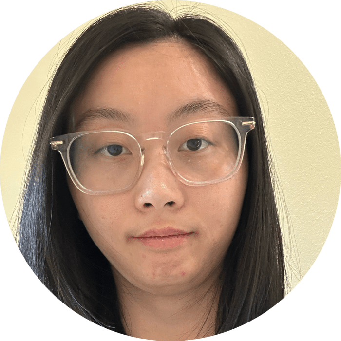 A person with long dark hair and clear glasses looks at the camera with a neutral expression, standing against a light-colored background—reminiscent of a calm and welcoming setting often found in Brooklyn Therapy sessions.