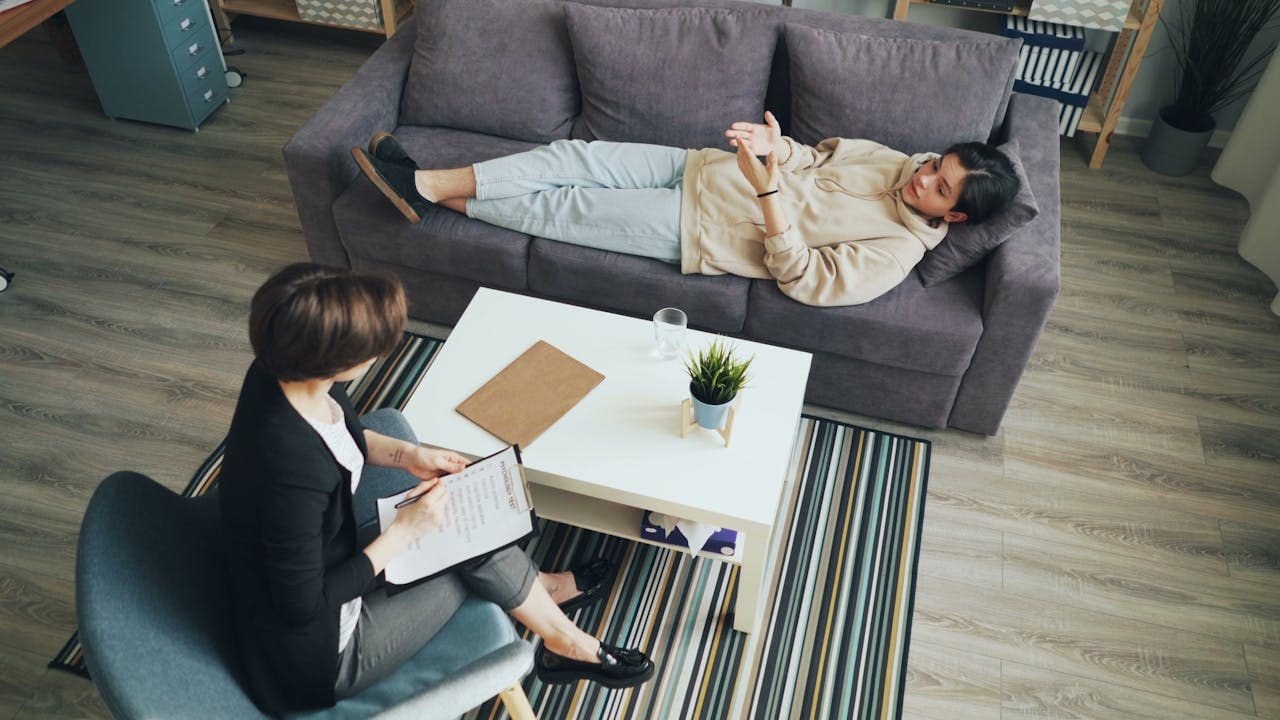 A person lies on a couch talking to a therapist nyc who takes notes on a clipboard; they are in a modern office with a coffee table between them, embodying the calming atmosphere of Brooklyn Therapy.