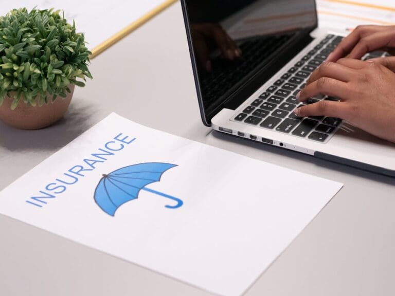 A person types on a laptop next to a document labeled “Insurance” with an umbrella icon, while a potted plant sits on the desk—illustrating the organized workspace of someone seeking therapy or connecting with a therapist in NYC, perhaps even scheduling Brooklyn Therapy sessions.