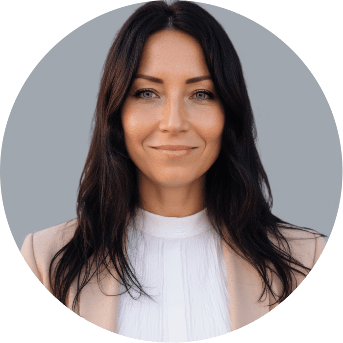 Woman with long dark hair, wearing a white blouse and beige blazer, smiles softly in a professional headshot against a plain gray background—capturing the approachable warmth you’d expect from a dedicated Brooklyn Therapy specialist and trusted therapist in NYC.