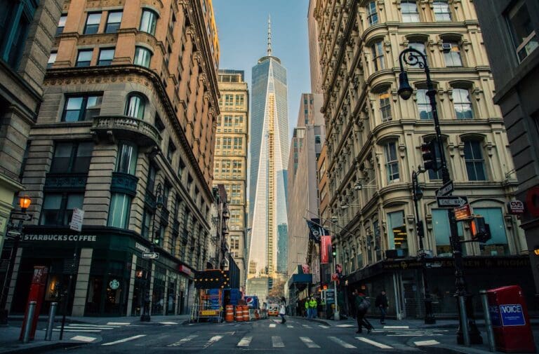 A wide city street with tall historic buildings on either side, leading to a modern glass skyscraper in the background on a clear day—an inviting scene that captures the blend of old and new, much like Brooklyn Therapy offers both timeless support and modern techniques for those seeking therapy in NYC.
