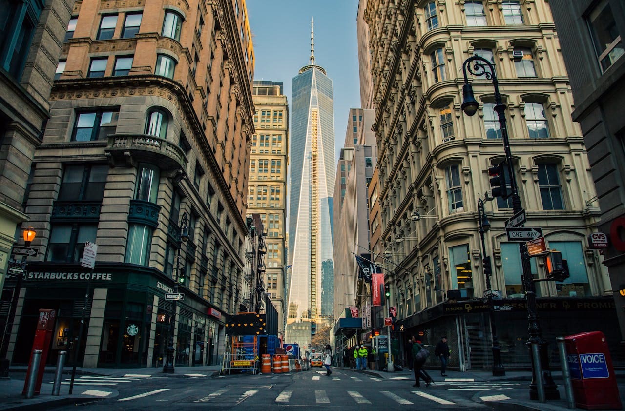 A wide city street with tall historic buildings on either side, leading to a modern glass skyscraper in the background on a clear day—an inviting scene that captures the blend of old and new, much like Brooklyn Therapy offers both timeless support and modern techniques for those seeking therapy in NYC.