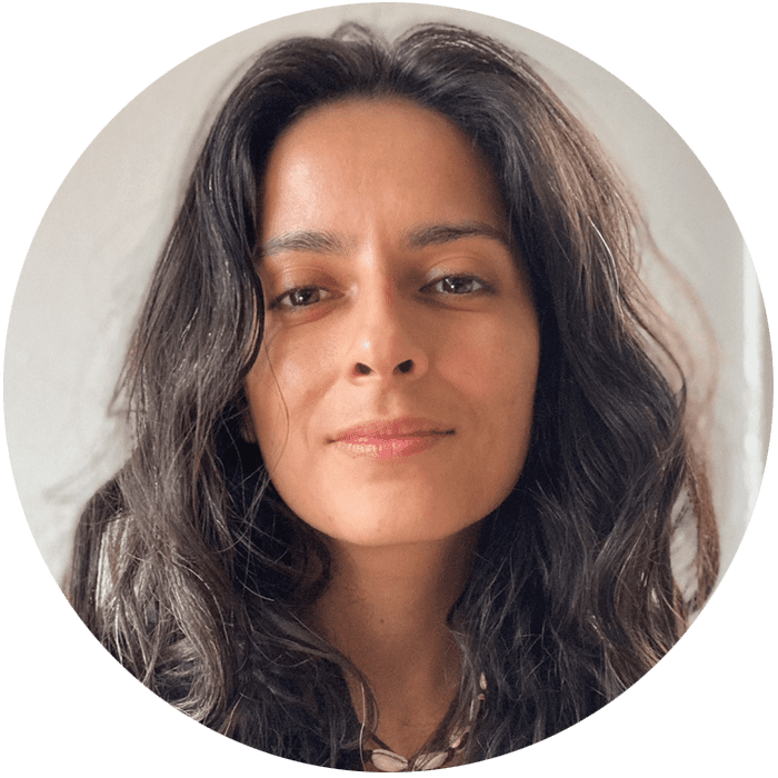 Woman with long wavy dark hair and a neutral expression, looking directly at the camera against a plain light background—reflecting the calm, approachable presence often sought in a therapist NYC or Brooklyn Therapy setting.