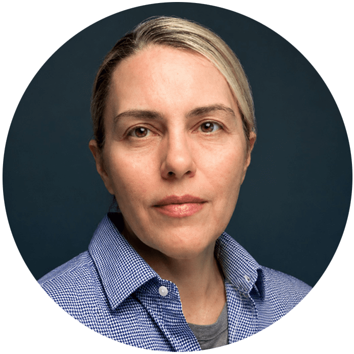 Person with light skin, short blonde hair, and a neutral expression, wearing a blue checkered shirt and gray undershirt, posed in front of a dark blue background—an approachable presence reflective of someone you might meet during Brooklyn Therapy sessions or while searching for a therapist in NYC.
