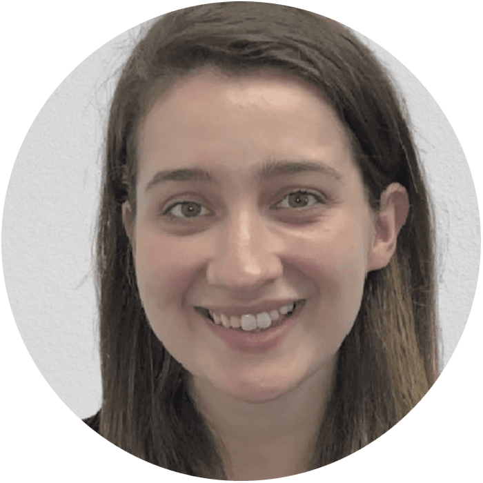 A woman with straight brown hair smiles at the camera. She is in front of a plain light-colored background, representing the welcoming atmosphere often found in Brooklyn Therapy sessions for those seeking a therapist in NYC.