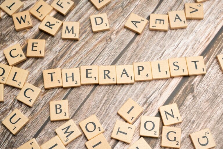 Scrabble tiles on a wooden surface spell “THERAPIST” in a row, surrounded by other scattered letter tiles, evoking the thoughtful process of therapy. This inviting scene captures the supportive environment fostered by Brooklyn Therapy and therapist NYC professionals.