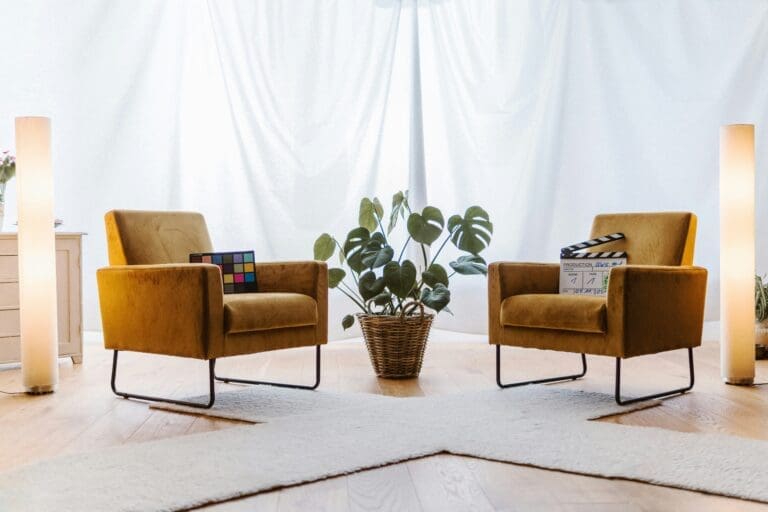 Two mustard-yellow armchairs face each other with a plant in between, set on a light rug with two tall lamps on either side—creating an inviting space reminiscent of a Brooklyn Therapy office, perfect for meaningful conversations and comfortable therapy sessions.