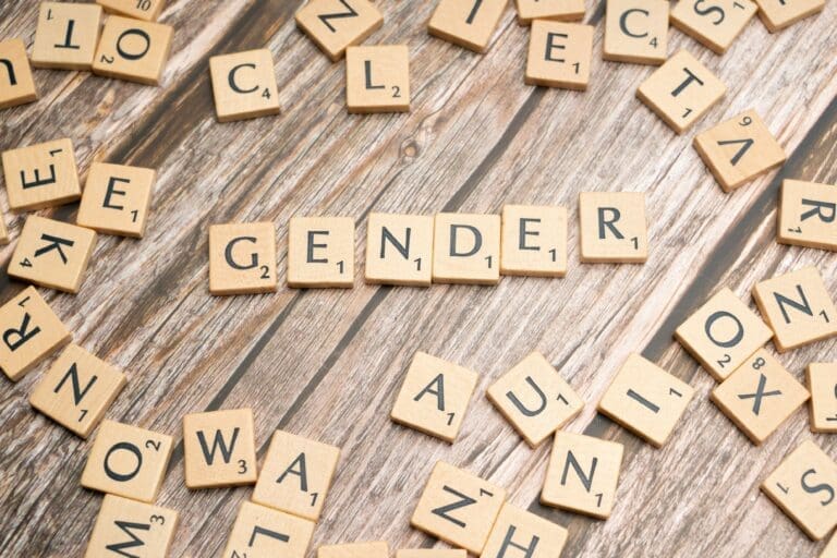 Scrabble tiles spelling “GENDER” are arranged on a wooden surface, surrounded by scattered letter tiles, evoking the thoughtful exploration often found in therapy or Brooklyn Therapy sessions.
