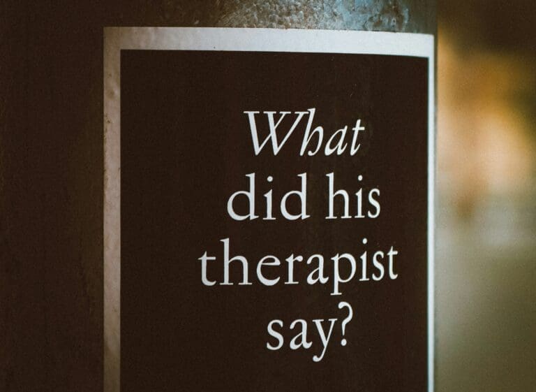 A black sign with white text reads, “What did his therapist say?” attached to a vertical surface—a playful nod to the culture of therapy in NYC and Brooklyn Therapy conversations.