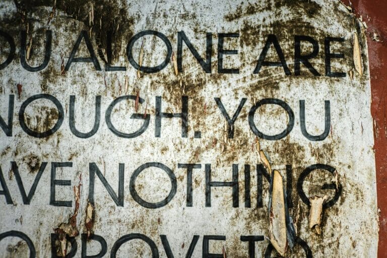 Close-up of a weathered and peeling sign with large black text partially reading, “ALONE ARE NOUGH. YOU HAVE NOTHING.” The surface shows dirt and damage—an image that echoes the challenges many face before reaching out for Brooklyn Therapy or seeking a therapist in NYC for support.