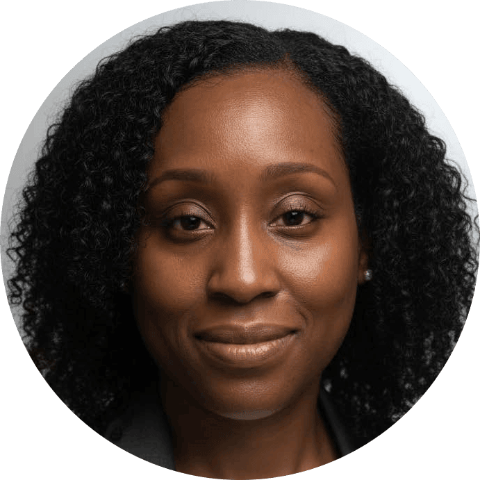 A woman with curly dark hair, medium brown skin, and a slight smile, facing forward against a plain light background—embodying the warmth and approachability often found in a therapist NYC clients trust for compassionate care.